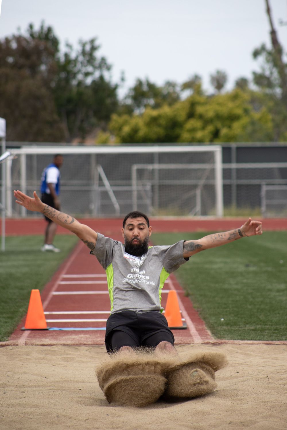 Competitor creates sandy splash during long jump landing on outdoor athletics track.