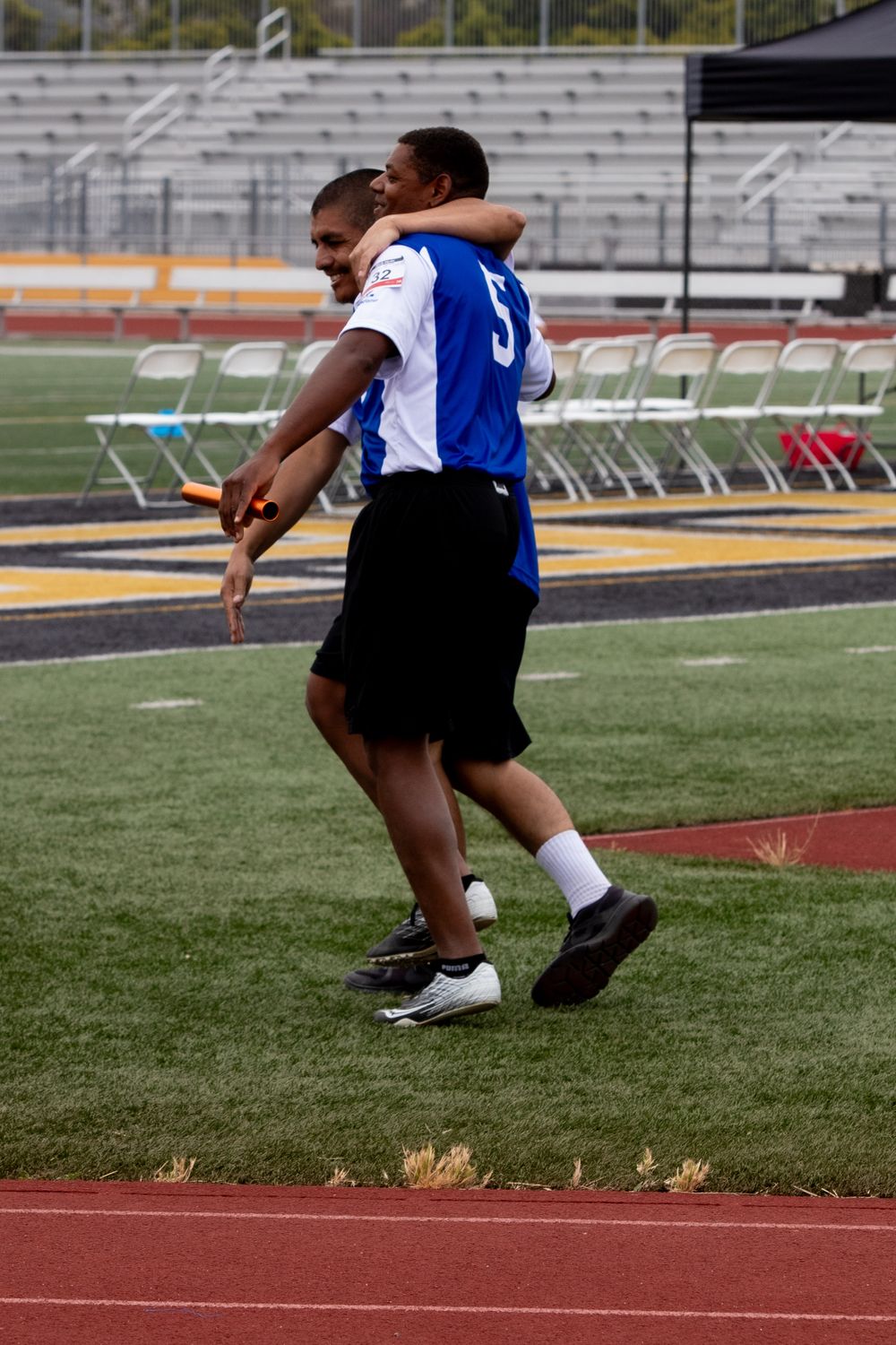 Athletes embrace after competition on athletic field with stadium bleachers in background.