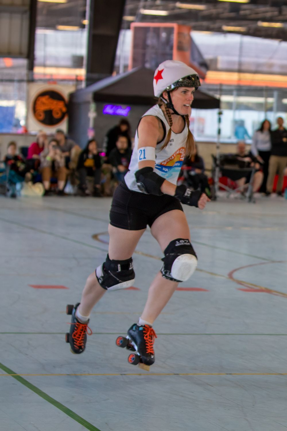 Roller derby athlete in protective gear skates during indoor competitive bout.