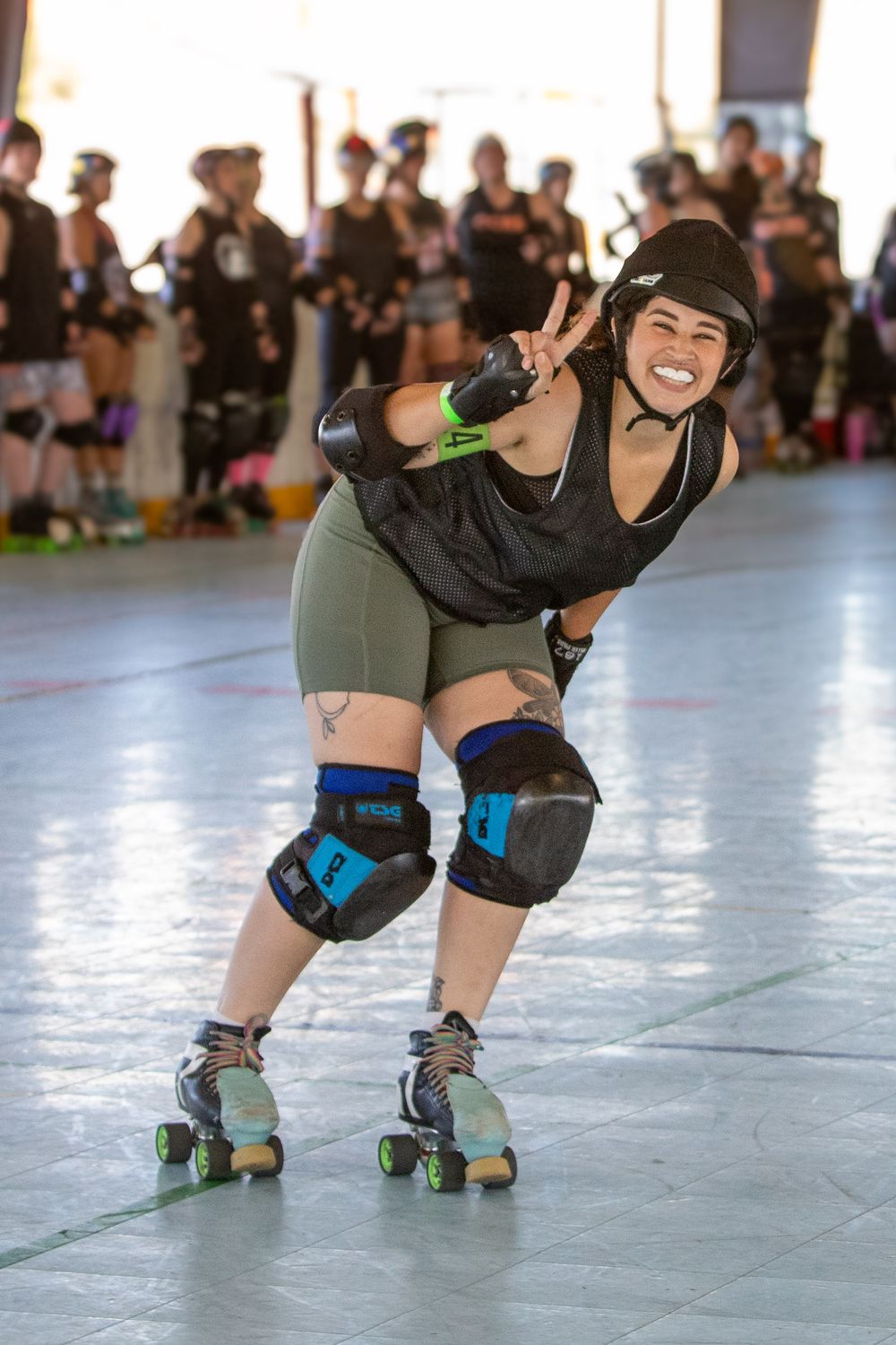 Roller derby skater in black shirt and olive shorts strikes a dynamic pose during practice.