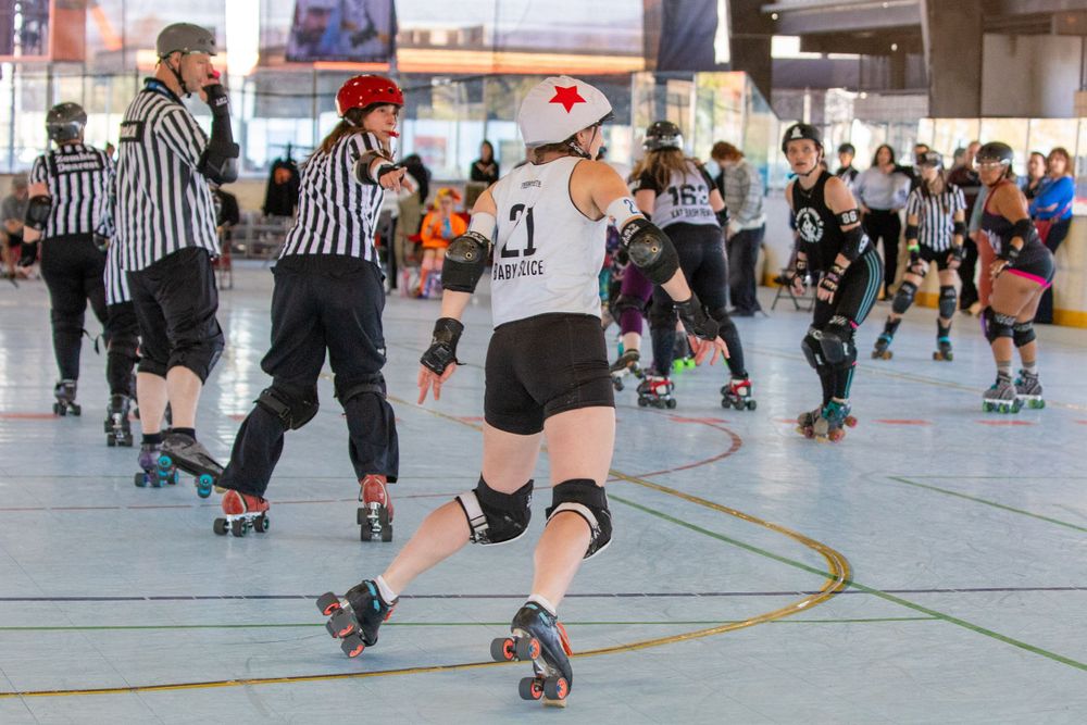 Roller derby match with referees and players racing around the track during a competitive bout.