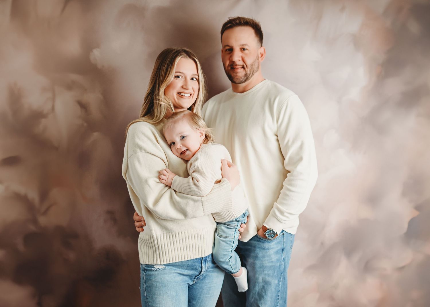 Family portrait session with soft brown backdrop and coordinated cream and blue outfits.