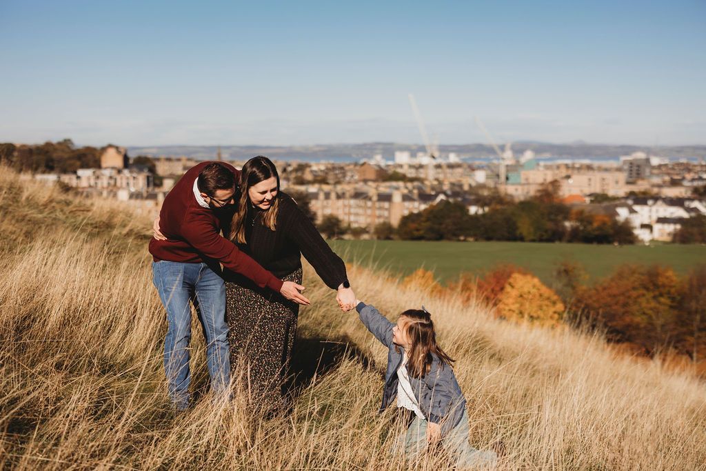 A group of people enjoy the outdoors on a grassy hillside overlooking an autumn cityscape on a sunny day.