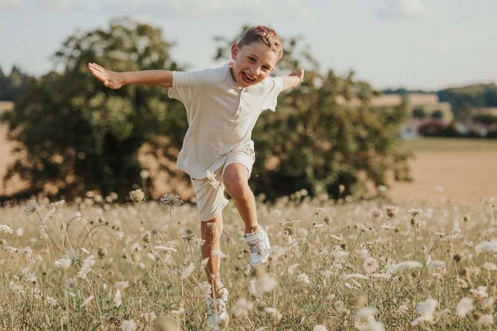 A person in white clothing stands in a sunlit meadow of white wildflowers on a summer afternoon.