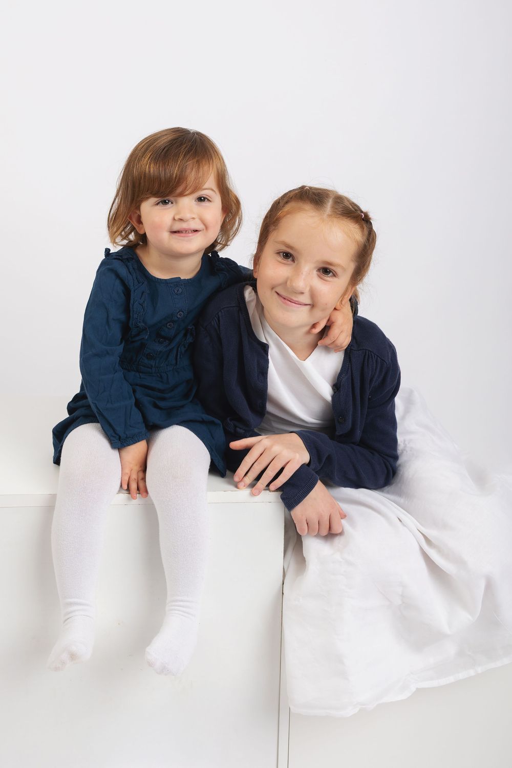 A sequence of four studio photos showing a child in navy blue and white sitting and lying on a white backdrop.