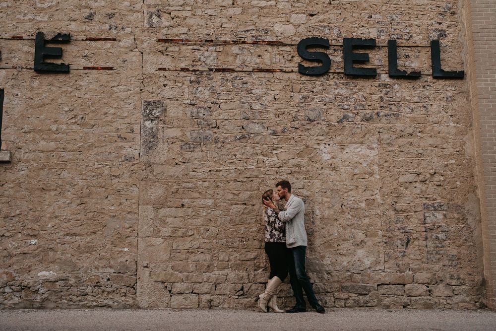 wide shot of couple kissing and embracing in front of an old factory stone wall