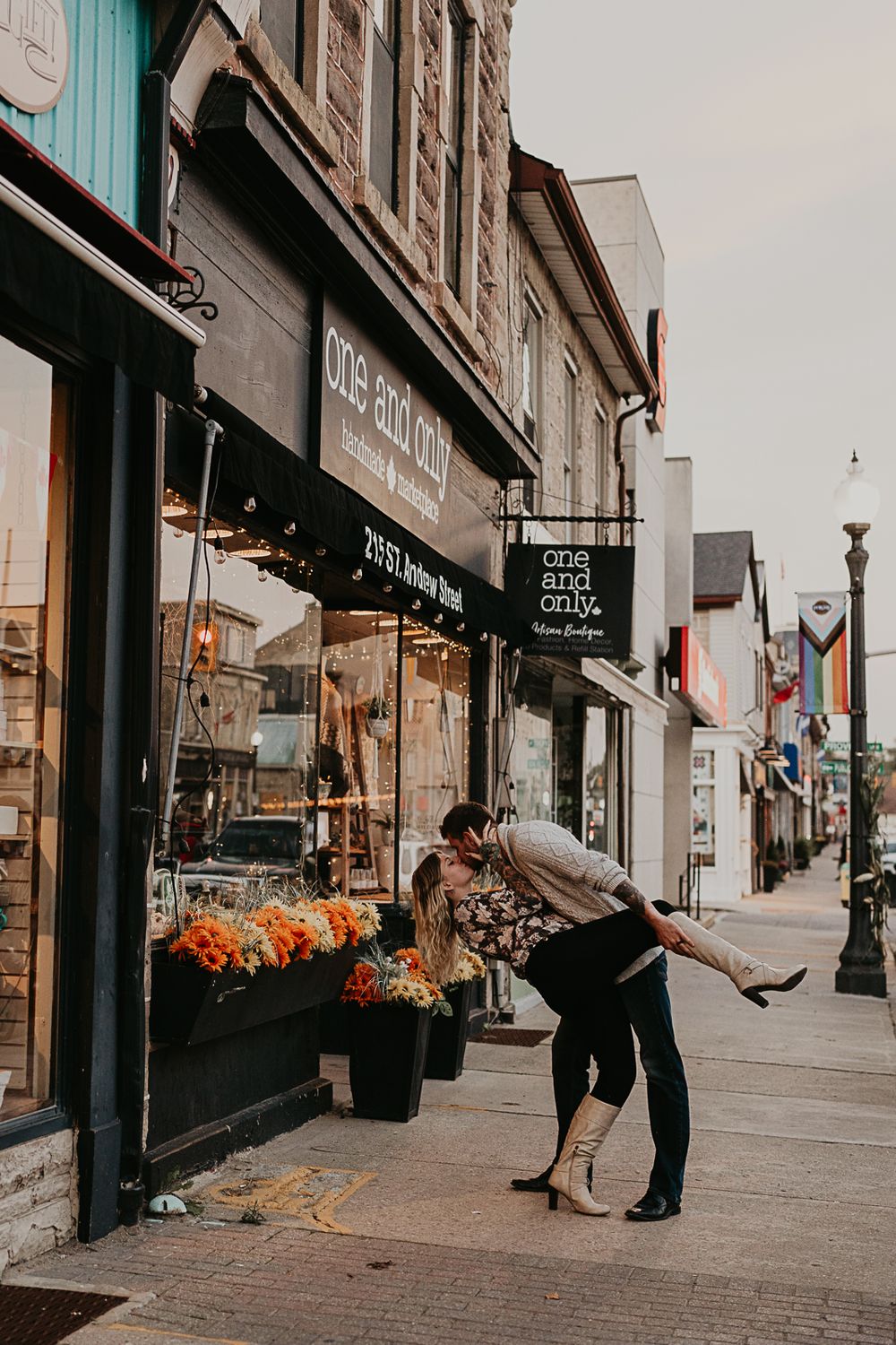 Man dips fiance as they kiss on street sidewalk near a shop with signage that say "one and only"