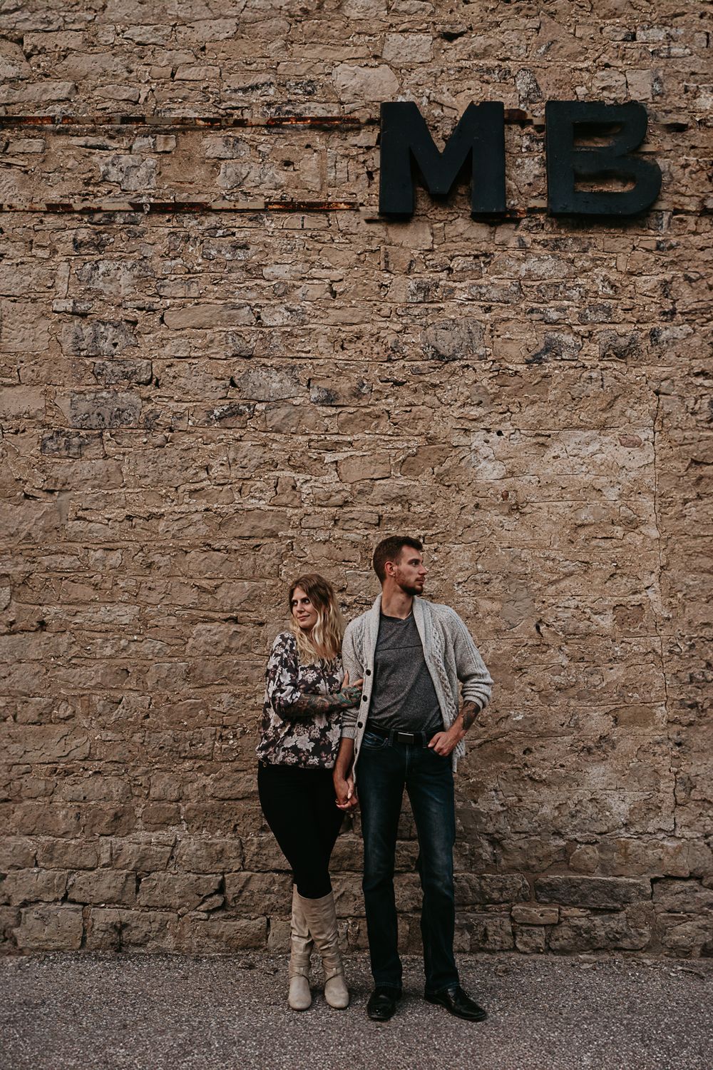 couple against old stonework wall with factory letters that spell out their initials "MB"