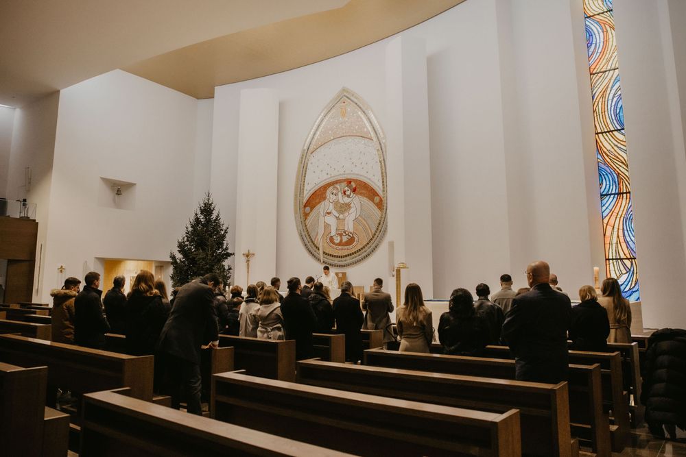 Interior of a modern church with white walls, pews, and a large circular religious mural at the altar.