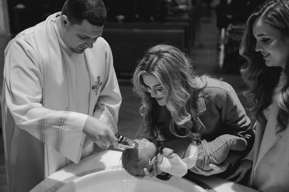 Black and white photo of a baptismal ceremony with participants gathered around the font.
