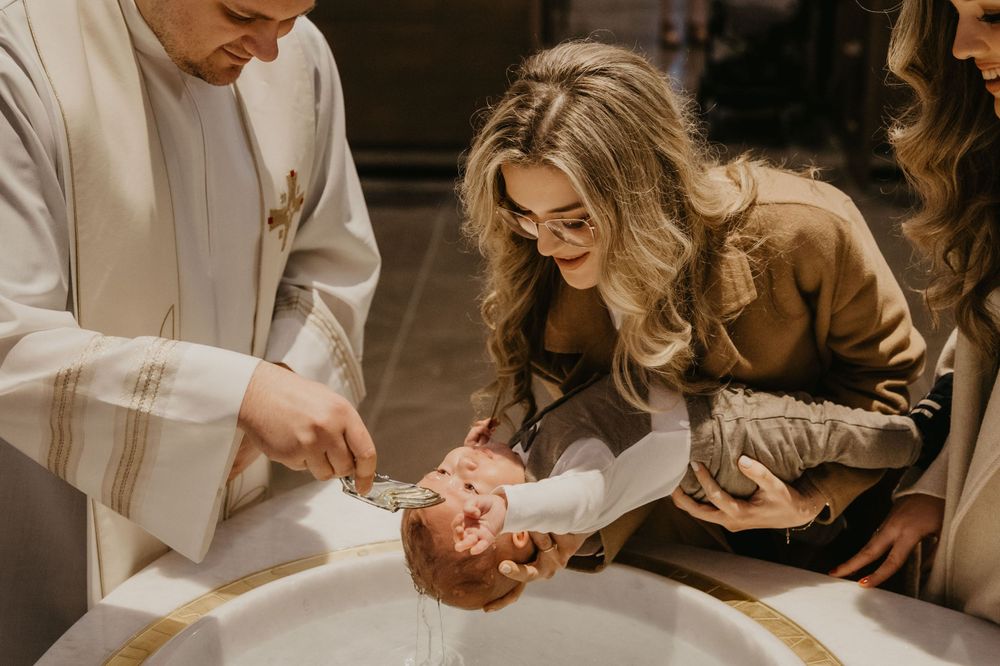 A baptism ceremony taking place with clergy and family gathered around the baptismal font.