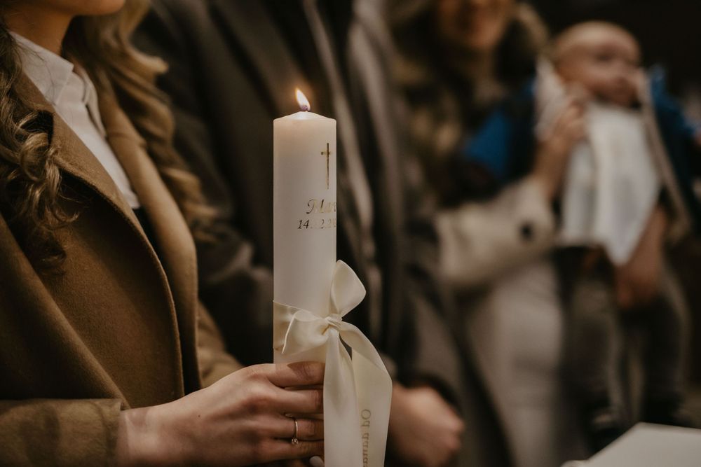 Someone holds a lit baptismal candle during a religious ceremony.