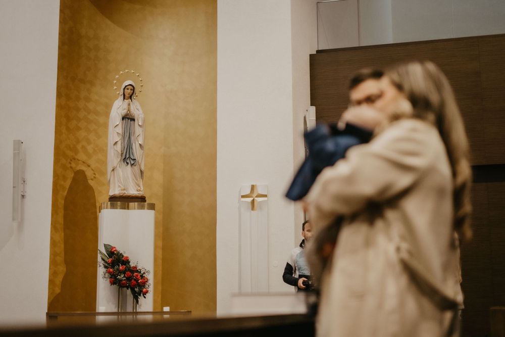 A statue of Mary in a church niche with ceremony participants in the foreground.