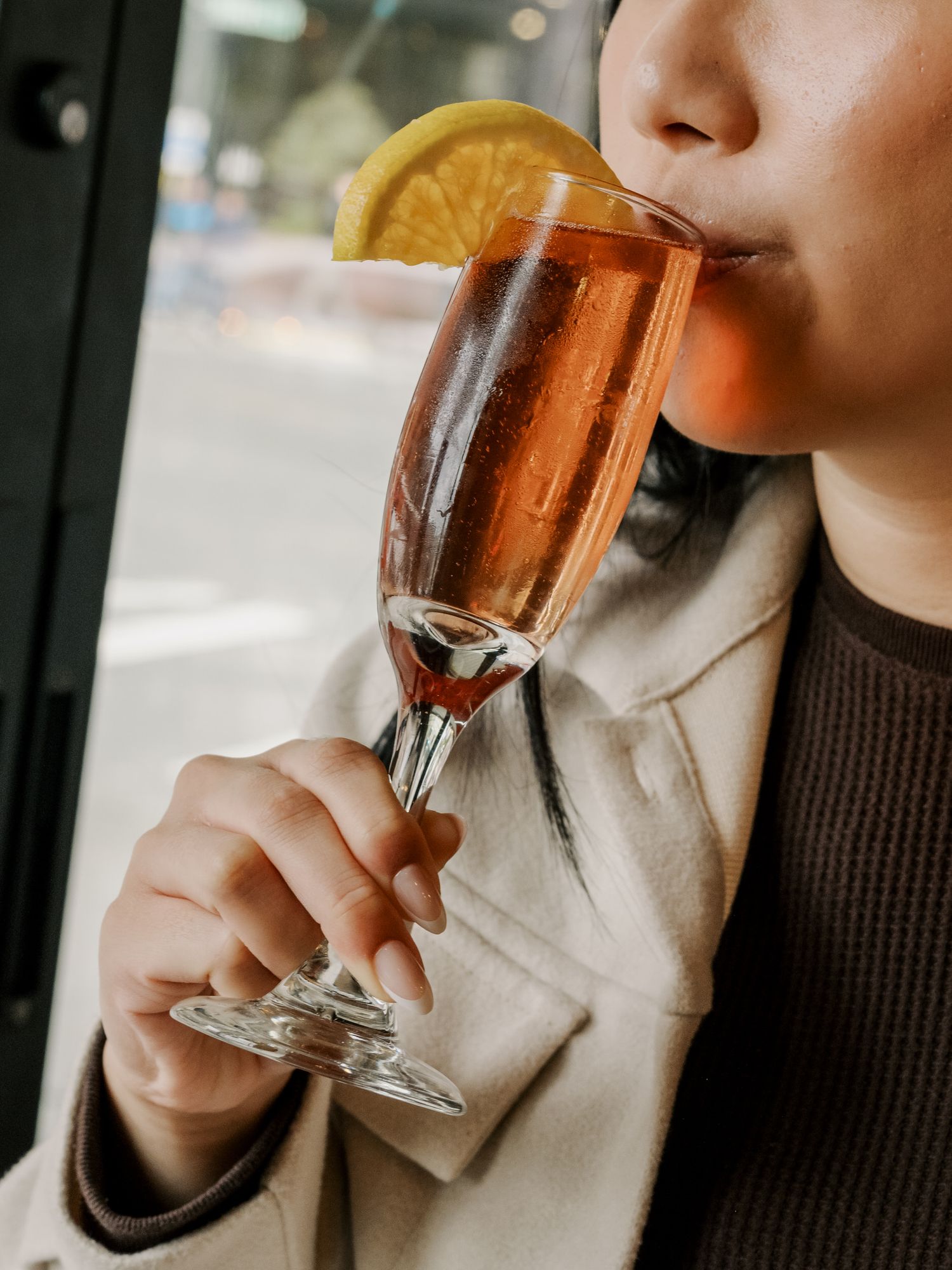 Someone sips a champagne cocktail garnished with an orange slice from an elegant fluted glass.