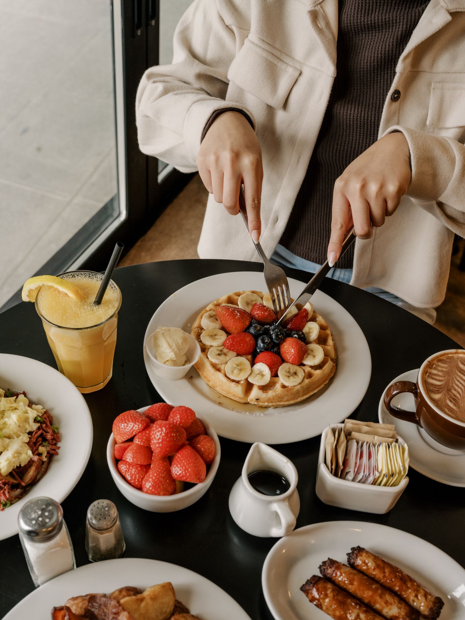 Overhead view of breakfast spread with waffles, berries, coffee, orange juice and french toast on dark table.
