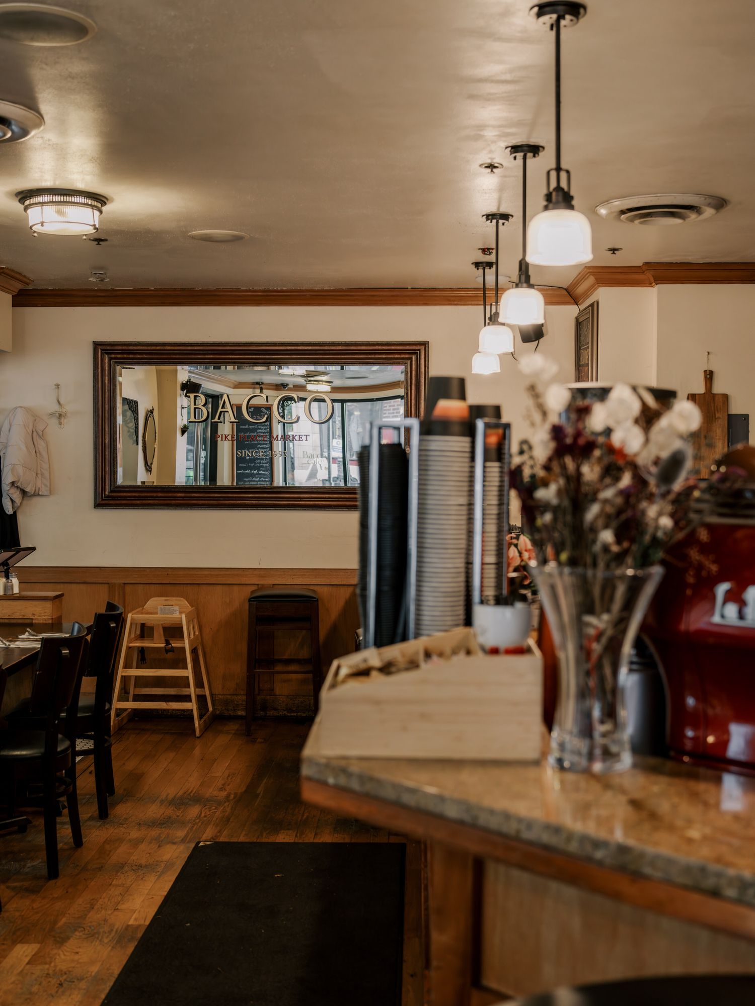 Cozy cafe interior with wooden floors, pendant lights, and a large mirror on the wall creating a warm atmosphere.