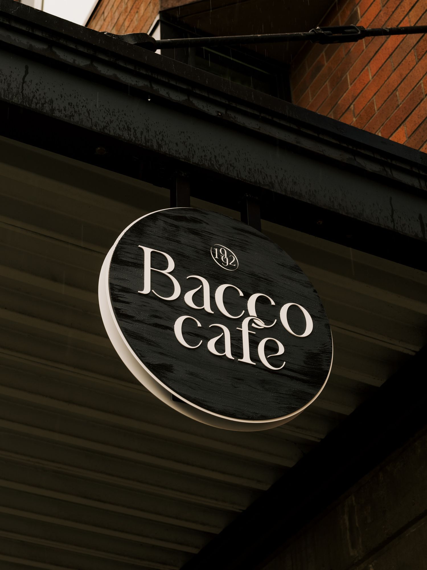 A black circular sign for 'Bacco Cafe' mounted on a dark wooden exterior wall.