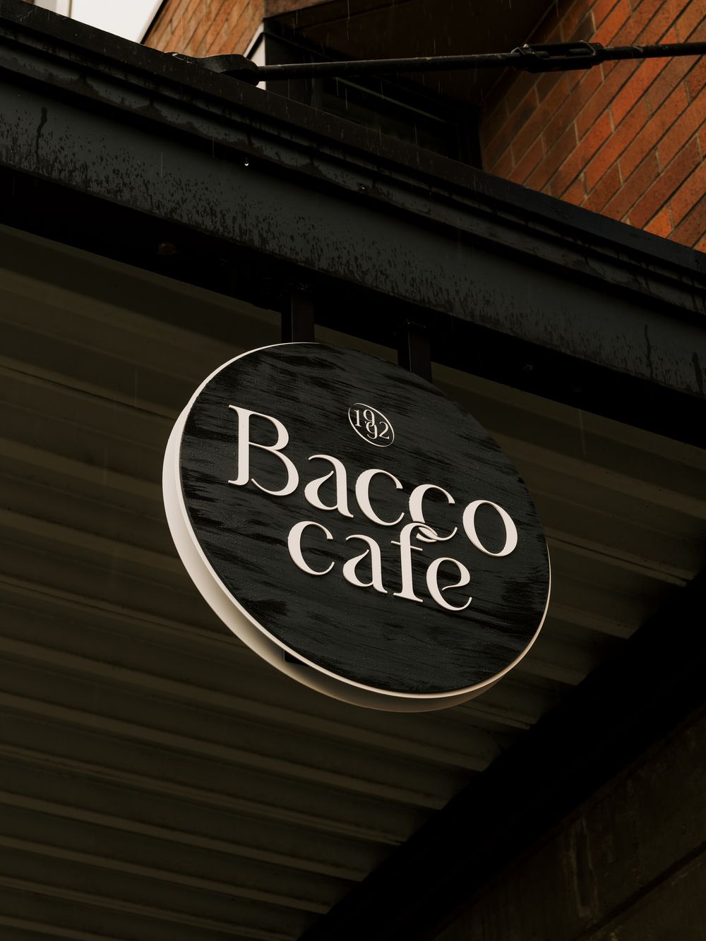 A black circular sign for 'Bacco Cafe' mounted on a dark wooden exterior wall.