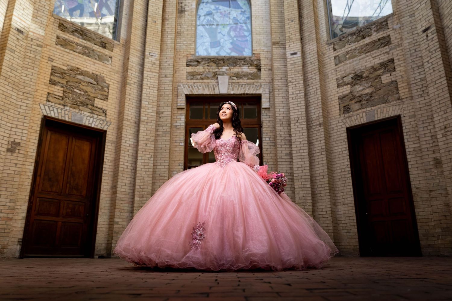 A dramatic pink ballgown photographed within historic stone architecture.