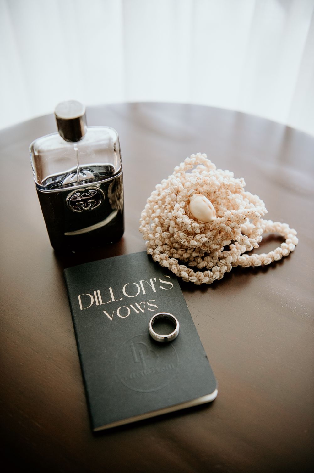 Wedding vow book with perfume bottle, ring and pearl necklace on dark table.