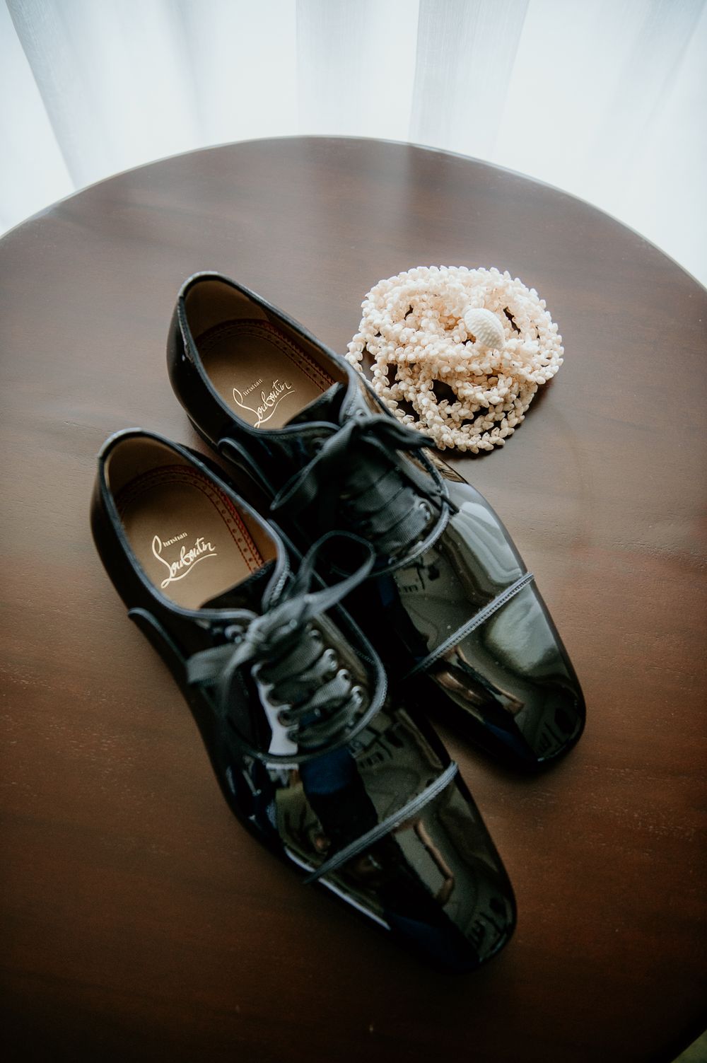 Shiny black patent leather dress shoes with pearl necklace on dark circular table.