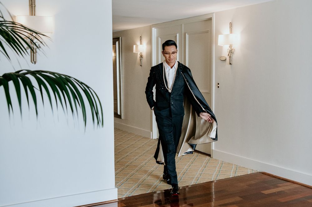 A formal black tuxedo and black cape ensemble captured in an elegant hotel hallway.