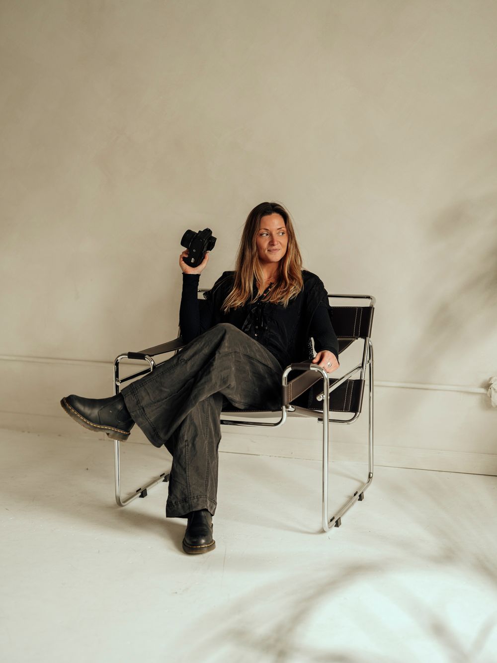 A person in a black shirt and gray pants sits casually in a modern white Wassily-style chair against a neutral background.