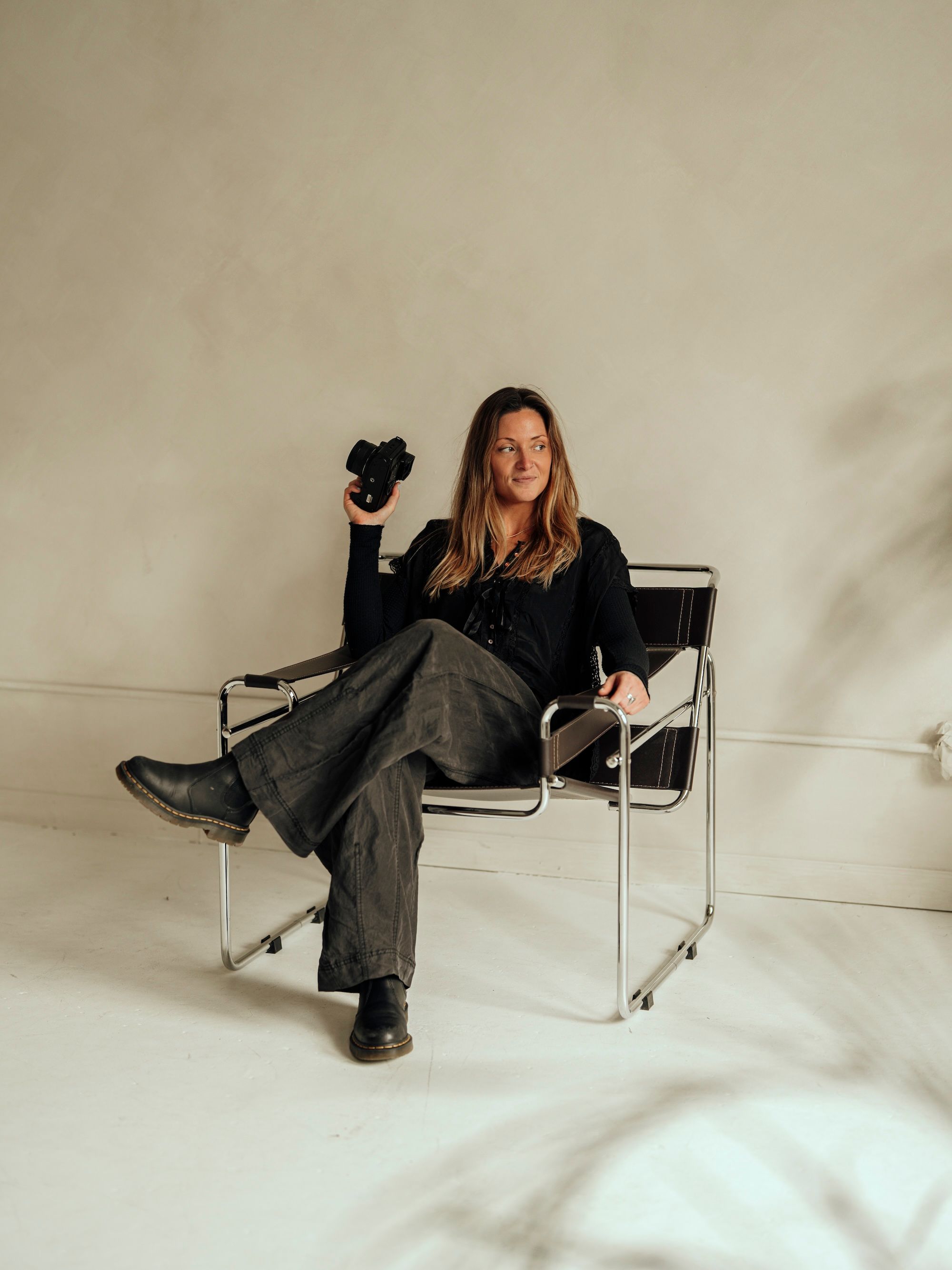 A person in a black shirt and gray pants sits casually in a modern white Wassily-style chair against a neutral background.