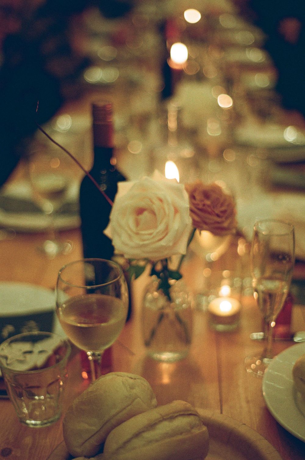 Elegant wedding reception table setting with roses, wine glasses and candlelight creating a romantic atmosphere.  Shot on 35mm film.
