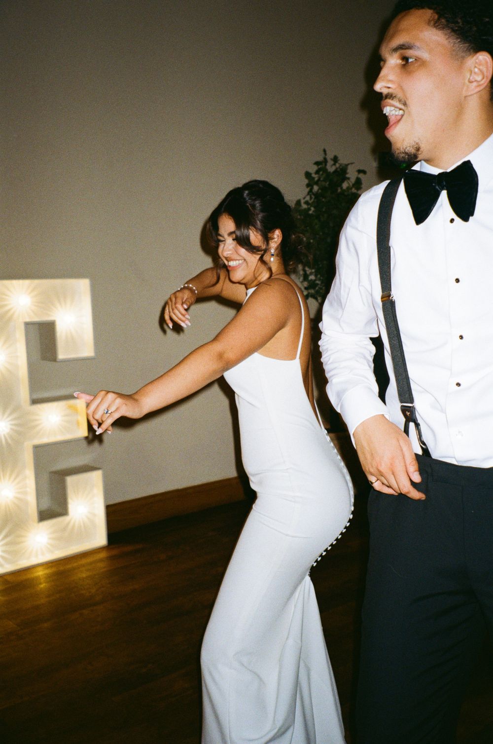 Wedding couple dancing energetically at their reception near illuminated decor.  Shot on 35mm film.