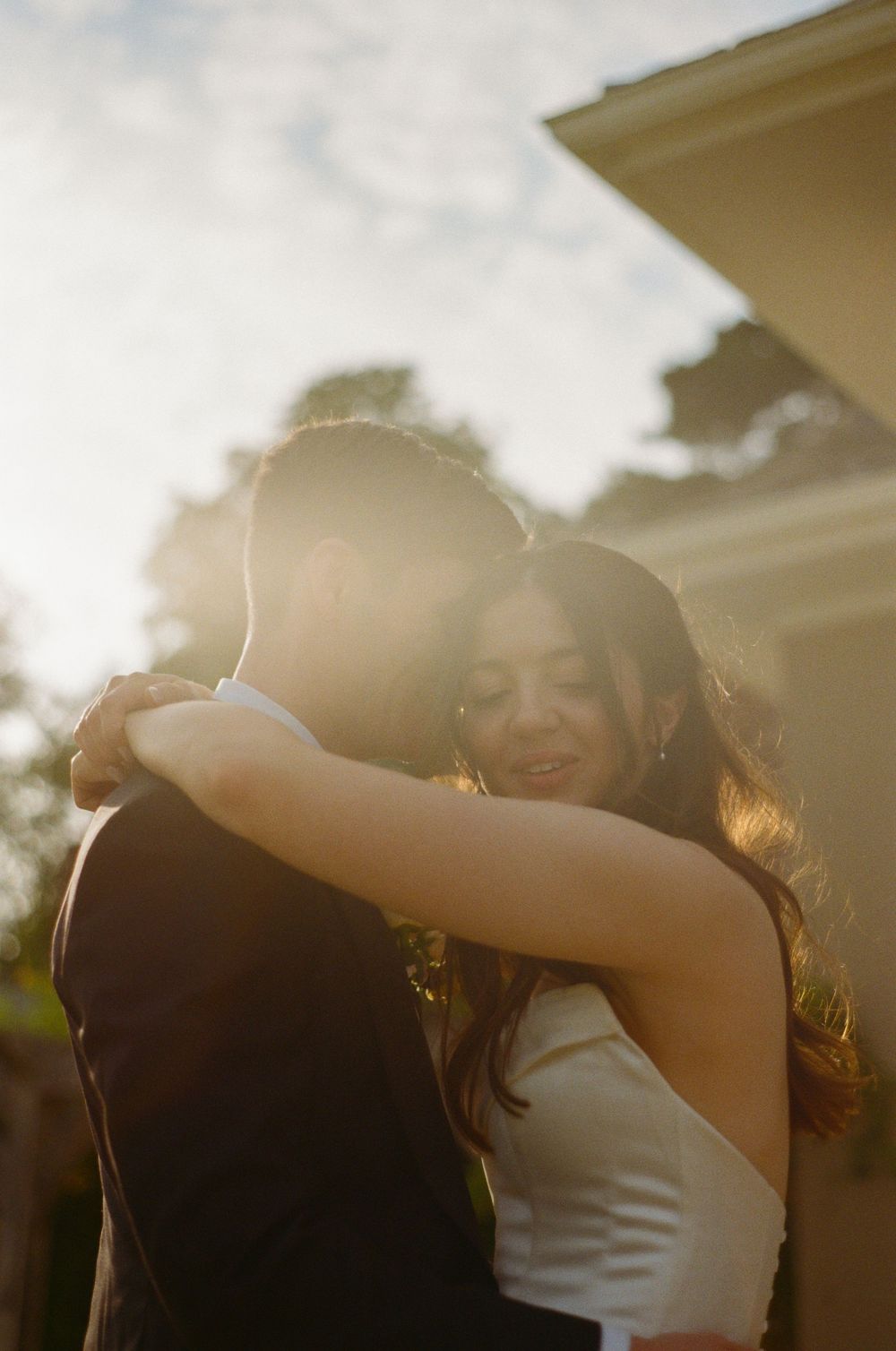 Sun flares illuminate a romantic embrace between two figures on a warm summer evening.
