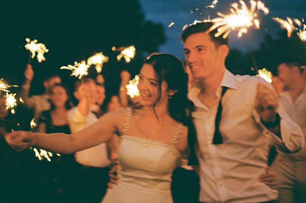 Wedding guests hold sparklers in their hands, creating a magical nighttime celebration atmosphere.