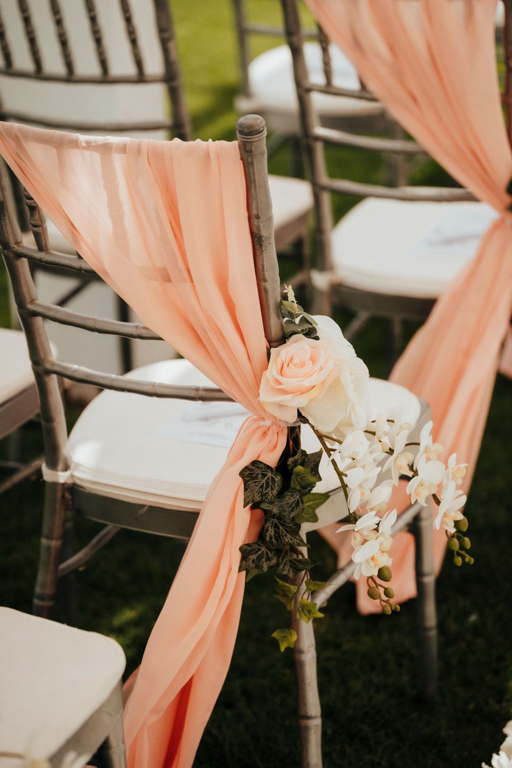 Wedding ceremony chair decorated with peach fabric draping and delicate white roses and greenery.