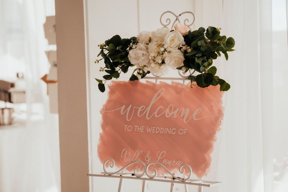 Romantic wedding welcome sign with coral watercolor background and white floral accents.