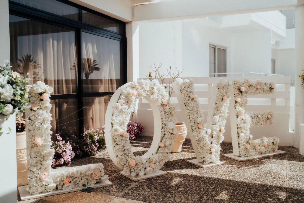 Large decorative 'LOVE' letters made of white flowers and dried foliage displayed against a light wall.