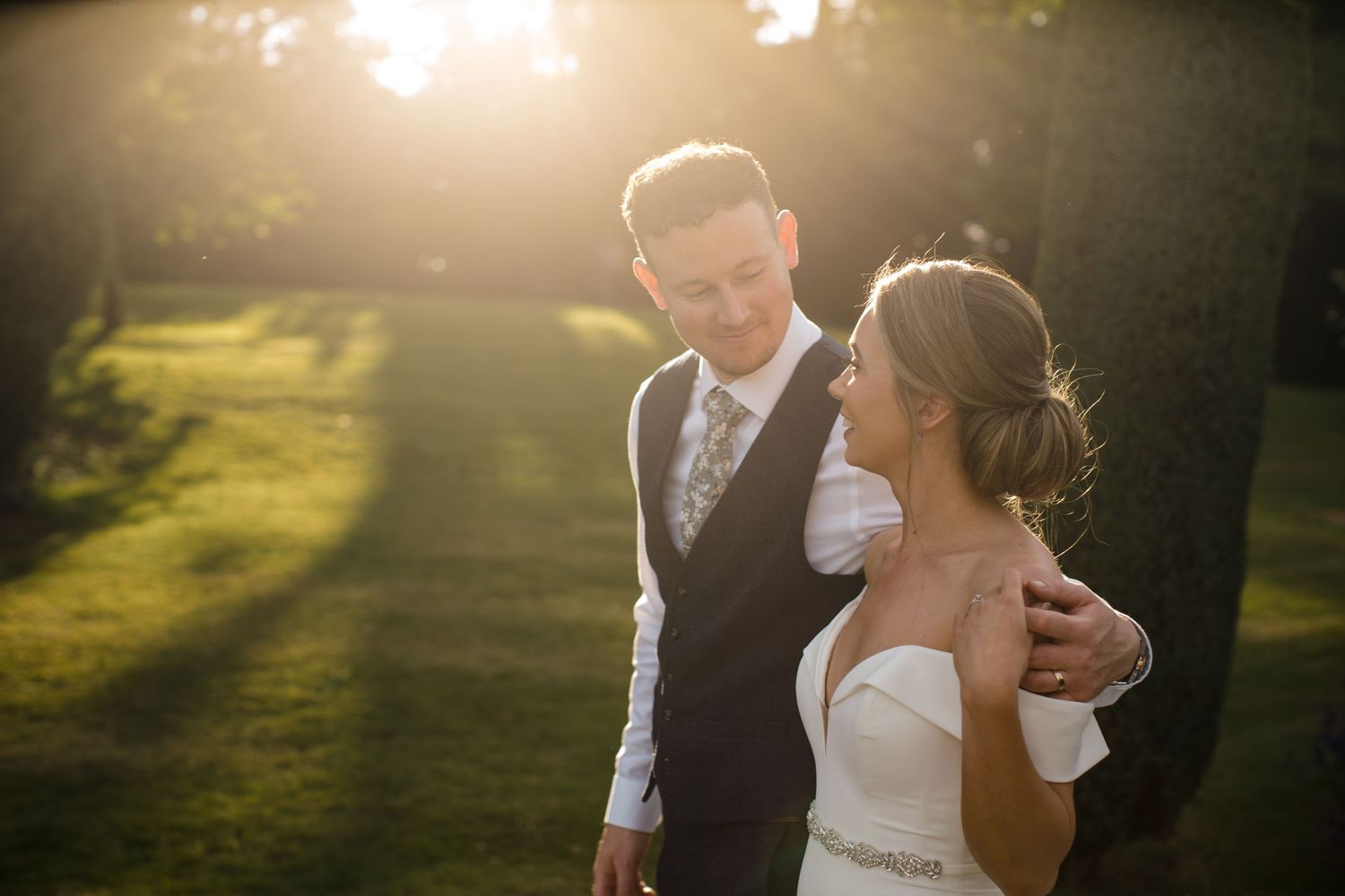 A couple in wedding attire share a tender moment on a lawn during golden hour with Nova Scotia wedding Photographer