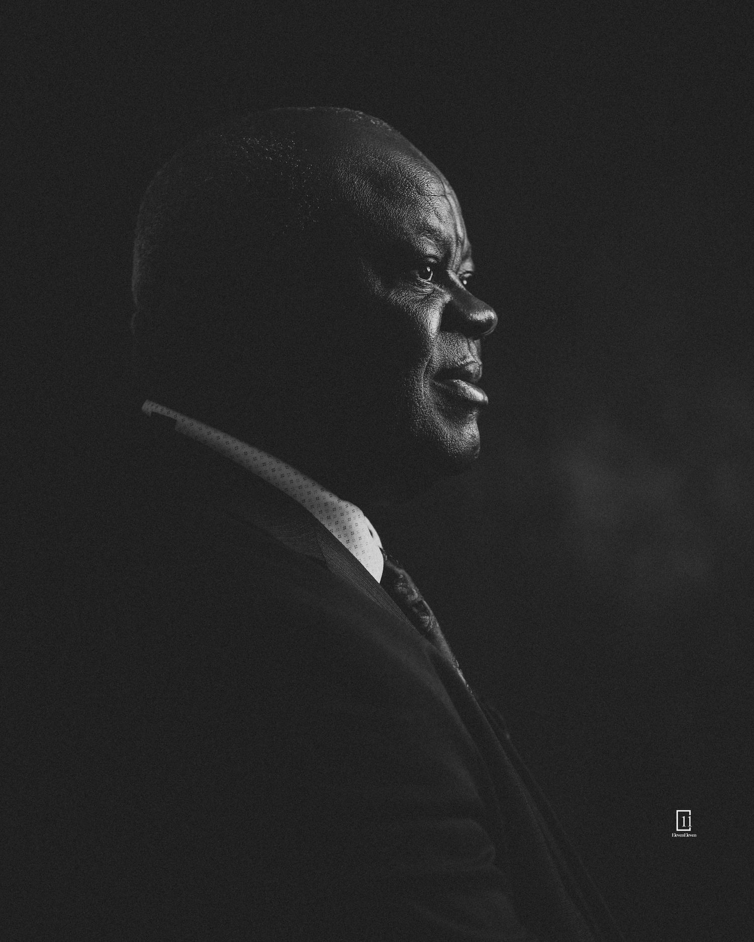 Dramatic black and white profile portrait with moody lighting and dark background.