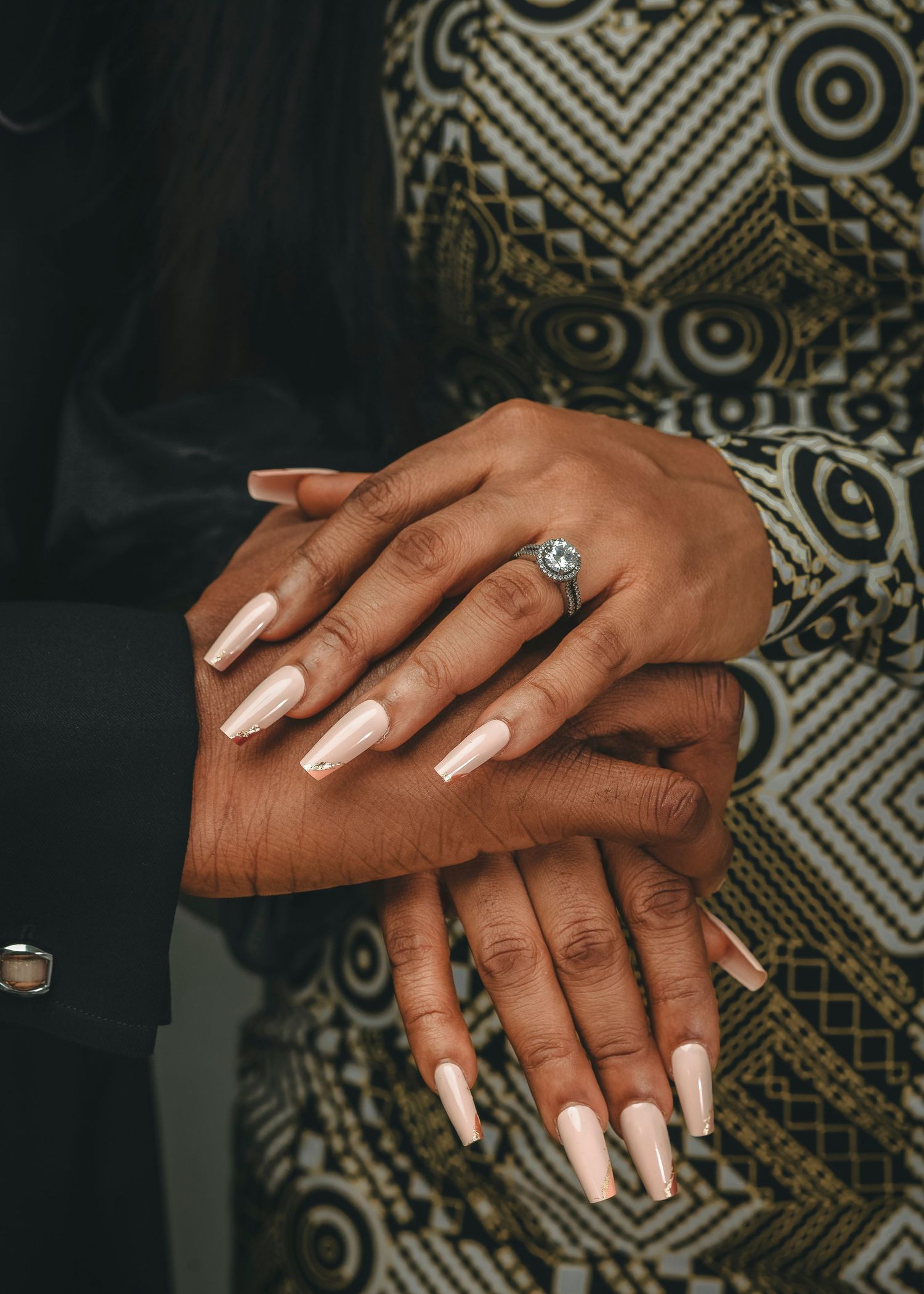 Elegant pearl white manicured nails and a sparkling engagement ring shown against a patterned background.