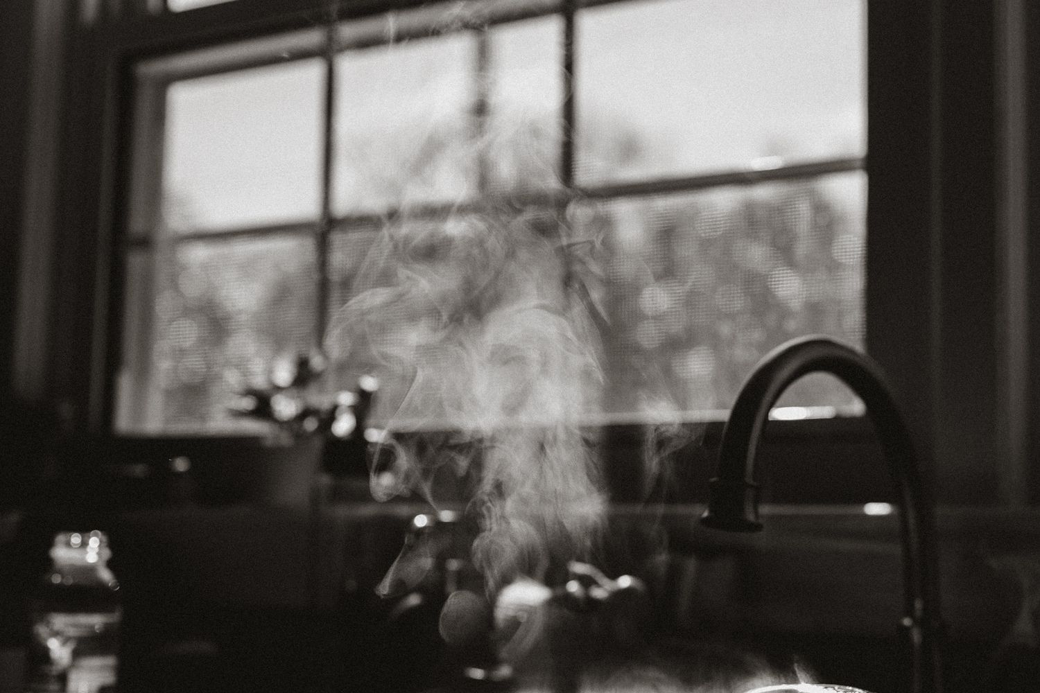 Steam rises from a hot sink near a window in a moody black and white photograph.
