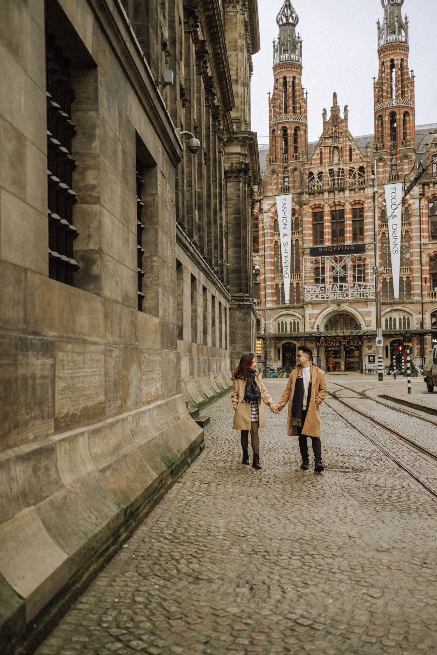 Couple in love at Dam Square with historic buildings in the background, standing alone in an empty street.