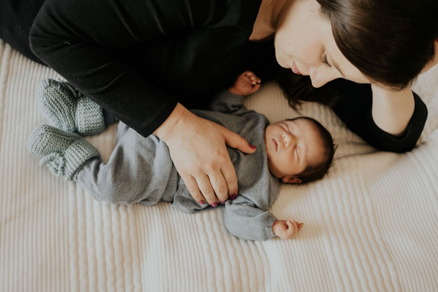 A tender moment between parent and baby lying together on white bedding.