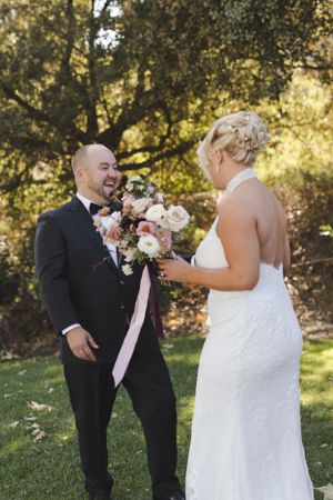 Couple sharing a joyful moment with floral bouquet during outdoor wedding ceremony.