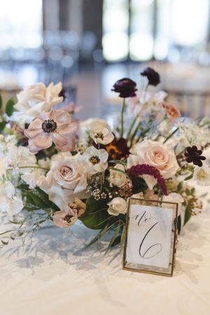 Elegant wedding table centerpiece with blush roses, burgundy flowers and gold frame table number on white tablecloth.