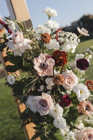 Beautiful floral arrangement with pink and burgundy roses, white anemones, and greenery against a sunny outdoor backdrop.