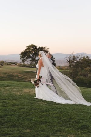 Flowing cathedral veil catches the breeze as sunset illuminates rolling hills in the background.