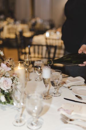Champagne being poured into glasses at an elegant table setting with floral centerpieces and candles.