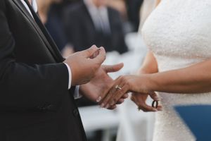 Close-up view of hands exchanging wedding rings during a marriage ceremony.