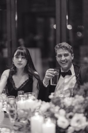 A couple in formal attire enjoying drinks at an elegant dinner party with floral centerpieces.