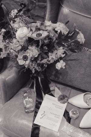 Black and white wedding details including a floral bouquet, invitation card, and bridal accessories on a chair.
