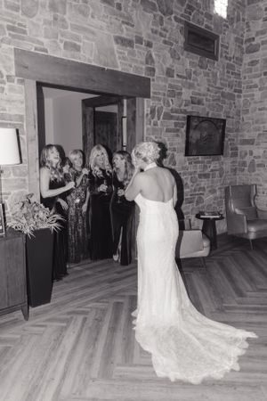Wedding party poses in elegant venue with stone walls and hardwood floors as bride shows off lace gown.